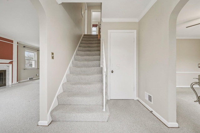 stairs with carpet floors, ornamental molding, and a premium fireplace