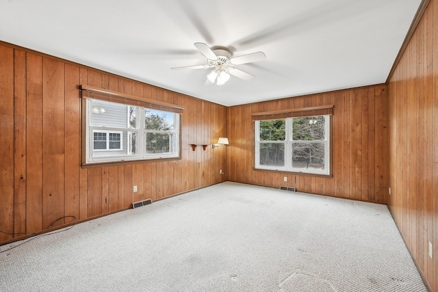 unfurnished room featuring light colored carpet, ceiling fan, and wood walls