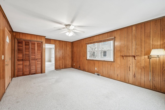 unfurnished bedroom featuring carpet, wooden walls, and ceiling fan