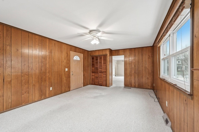 carpeted empty room with ceiling fan and wood walls