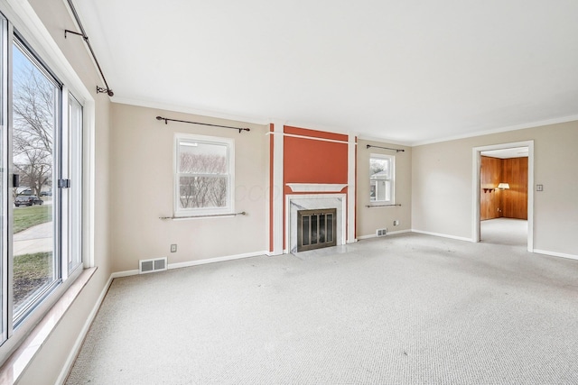 unfurnished living room with carpet floors, ornamental molding, a premium fireplace, and plenty of natural light