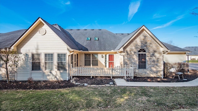 view of front of property featuring a front lawn, stone siding, and roof with shingles