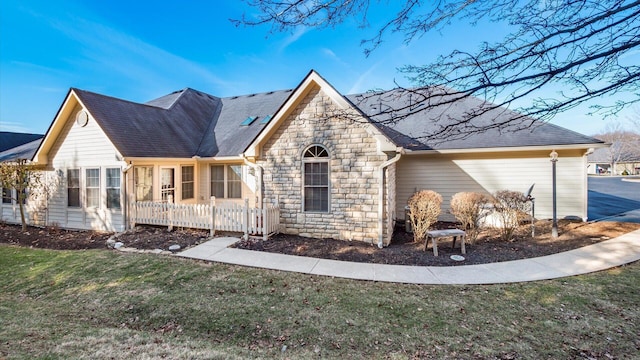 view of front of property with stone siding, a front lawn, and roof with shingles