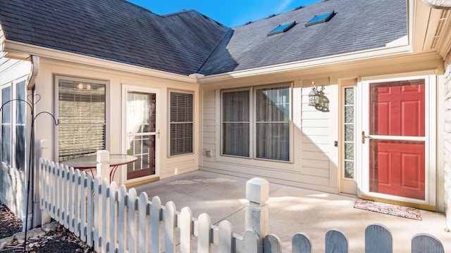 entrance to property featuring roof with shingles and fence