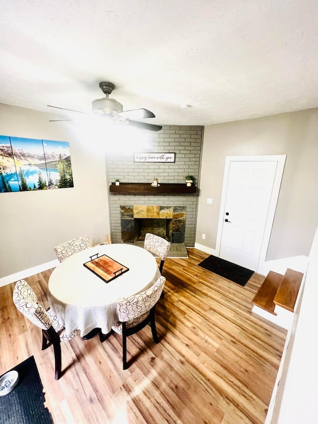 dining area featuring ceiling fan, a brick fireplace, hardwood / wood-style floors, and a textured ceiling