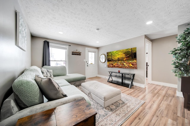 living room featuring light wood-style floors, a textured ceiling, and baseboards