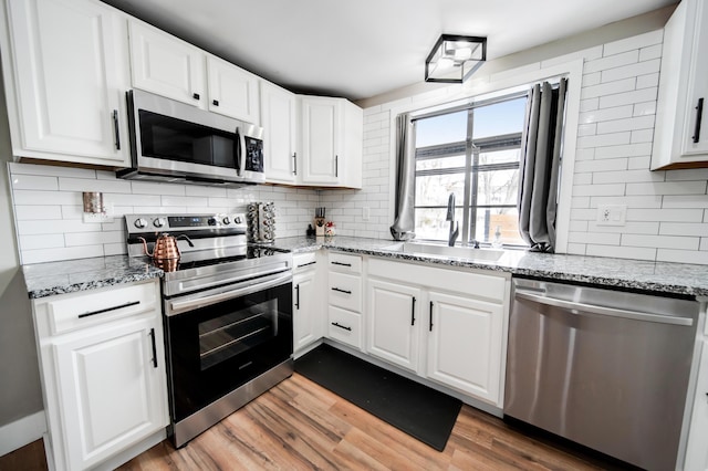 kitchen with light stone counters, appliances with stainless steel finishes, white cabinets, a sink, and wood finished floors