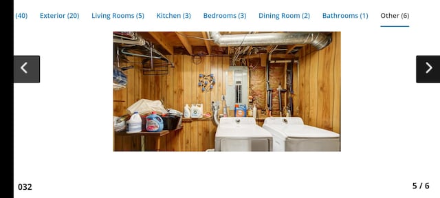 clothes washing area with wooden walls, electric panel, and washer and dryer