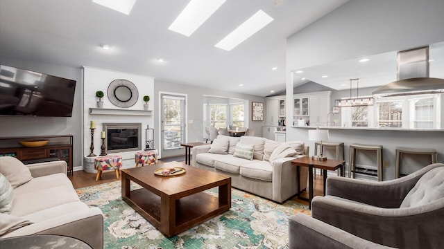 living room with a fireplace, light hardwood / wood-style flooring, sink, and vaulted ceiling with skylight