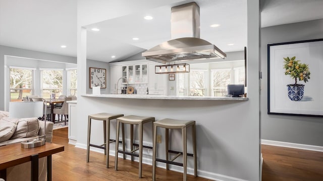 kitchen featuring white cabinetry, dark wood-type flooring, island range hood, and kitchen peninsula