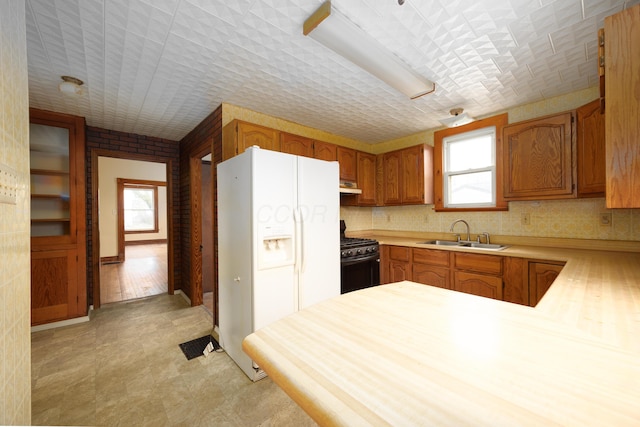 kitchen featuring sink, kitchen peninsula, black range with gas stovetop, and white fridge with ice dispenser