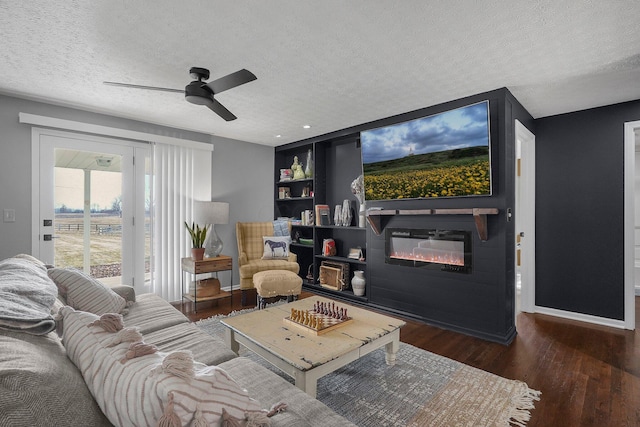 living room featuring a textured ceiling, wood finished floors, a glass covered fireplace, and a ceiling fan