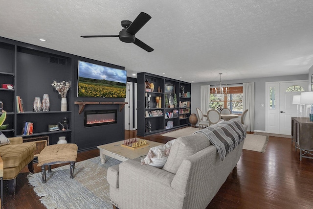 living area with built in features, a ceiling fan, a glass covered fireplace, a textured ceiling, and wood finished floors