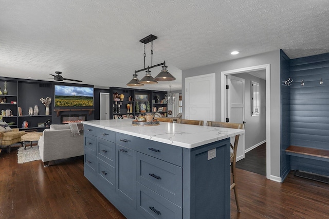 kitchen with light stone counters, a breakfast bar, a ceiling fan, dark wood-style floors, and a glass covered fireplace