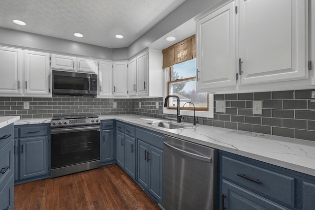 kitchen featuring dark wood-style floors, appliances with stainless steel finishes, blue cabinetry, white cabinetry, and a sink