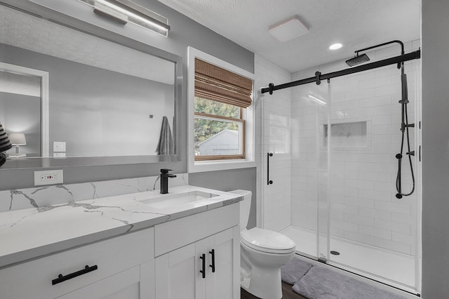 full bathroom featuring toilet, a stall shower, a textured ceiling, and vanity