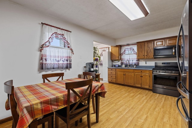 kitchen with stainless steel appliances, sink, a textured ceiling, and light hardwood / wood-style flooring