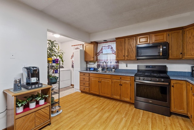 kitchen featuring washer / dryer, sink, light hardwood / wood-style flooring, and stainless steel gas stove