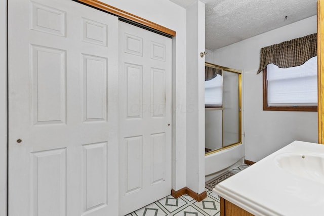 bathroom featuring bath / shower combo with glass door, vanity, and a textured ceiling