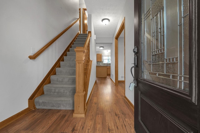 foyer entrance with baseboards, a textured ceiling, stairway, and wood finished floors