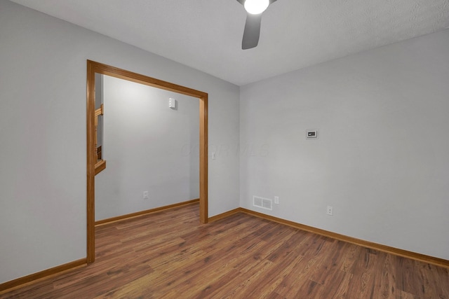 spare room featuring a ceiling fan, visible vents, baseboards, and wood finished floors