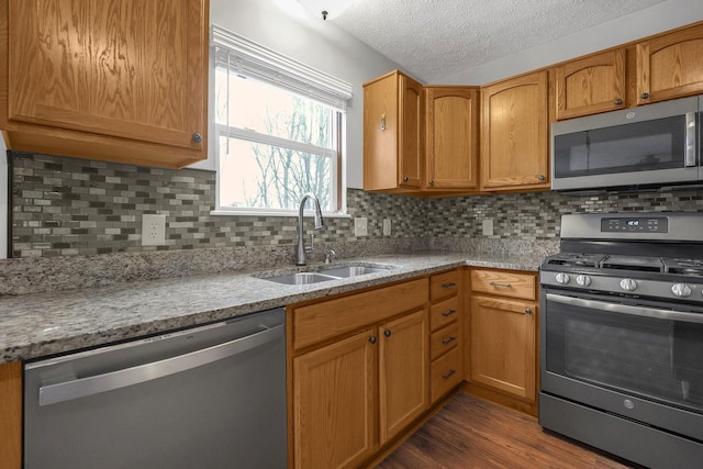 kitchen featuring a textured ceiling, stainless steel appliances, a sink, backsplash, and dark wood finished floors