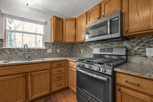 kitchen featuring a textured ceiling, light stone counters, a sink, appliances with stainless steel finishes, and dark wood-style floors