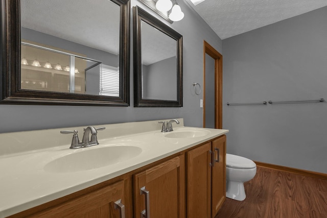 bathroom featuring double vanity, a textured ceiling, toilet, and a sink