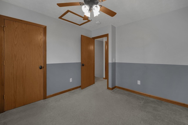 unfurnished bedroom with attic access, baseboards, a ceiling fan, and light colored carpet