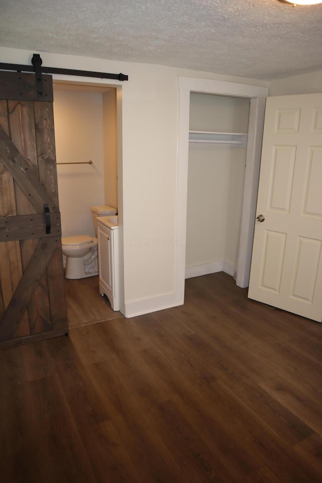 unfurnished bedroom featuring connected bathroom, a textured ceiling, dark hardwood / wood-style flooring, a closet, and a barn door