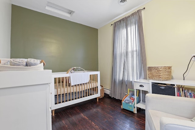 bedroom featuring a crib, a baseboard radiator, attic access, and dark wood-style flooring