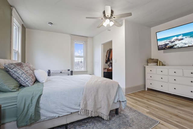 bedroom with ceiling fan, a spacious closet, light wood-style flooring, and baseboards