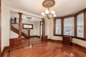 unfurnished dining area with hardwood / wood-style flooring, a chandelier, and ornate columns