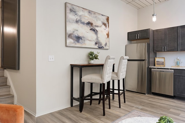 kitchen featuring dark brown cabinetry, decorative light fixtures, light hardwood / wood-style floors, and appliances with stainless steel finishes