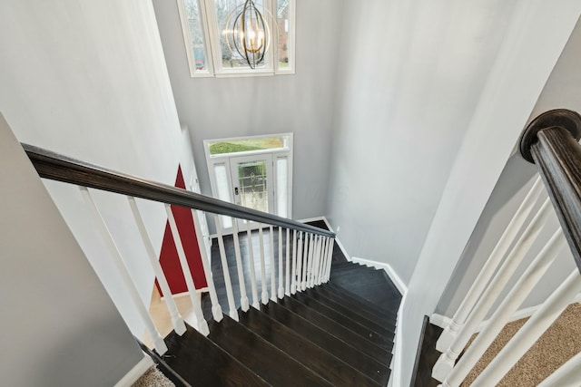 stairway with hardwood / wood-style flooring, a towering ceiling, and an inviting chandelier