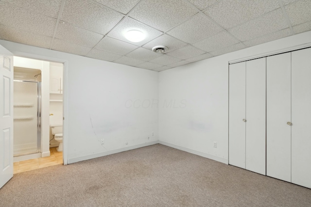 unfurnished bedroom featuring light carpet, ensuite bath, a paneled ceiling, and a closet