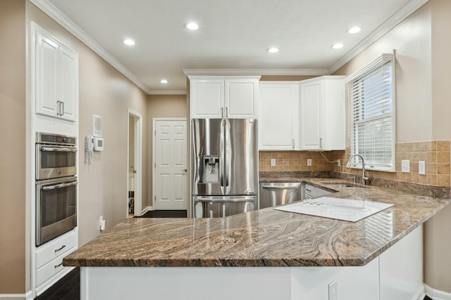 kitchen featuring sink, appliances with stainless steel finishes, white cabinetry, kitchen peninsula, and dark stone counters