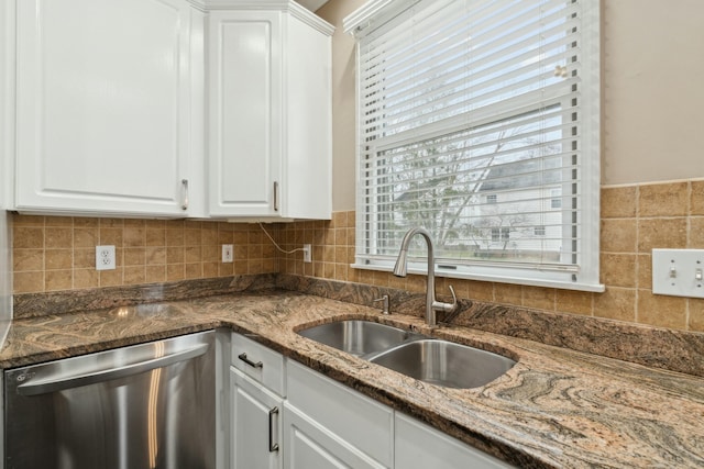 kitchen featuring sink, white cabinetry, stainless steel dishwasher, dark stone counters, and backsplash