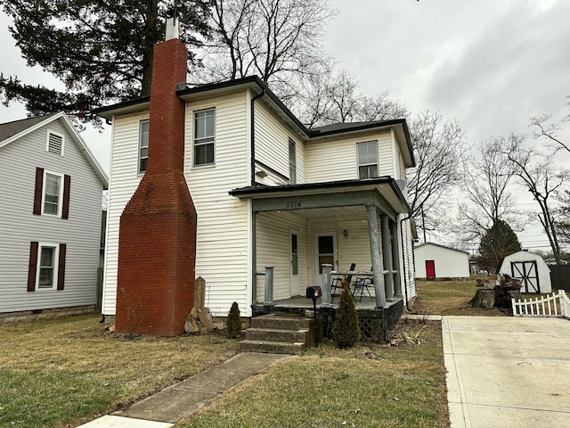 view of front of home featuring a storage unit, covered porch, and a front yard