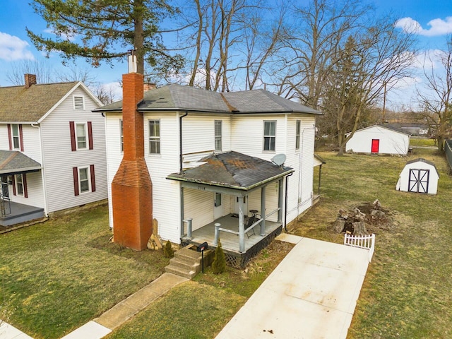 view of front of house featuring a porch, an outbuilding, a shingled roof, and a front lawn