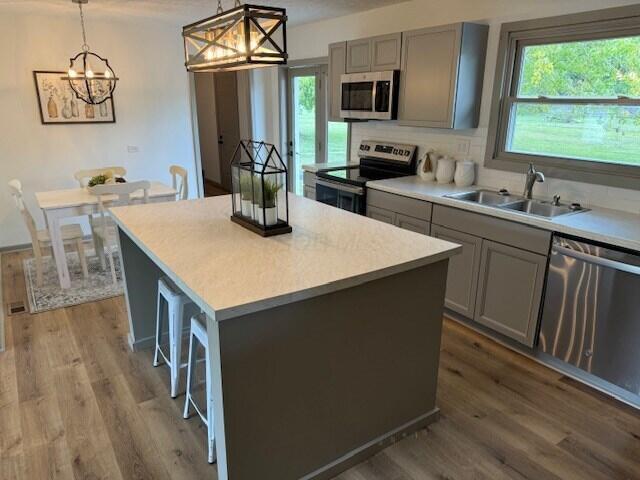 kitchen with sink, gray cabinetry, decorative light fixtures, a center island, and appliances with stainless steel finishes