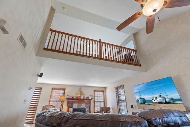 living room featuring a fireplace, ceiling fan, and a high ceiling