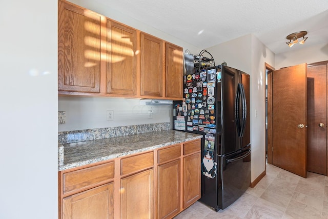 kitchen with light stone countertops, black refrigerator, and a textured ceiling