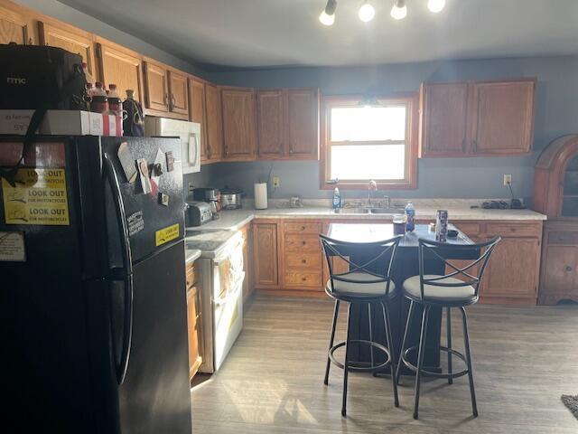 kitchen featuring sink, a breakfast bar area, black fridge, range, and light hardwood / wood-style floors