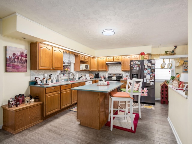 kitchen with stainless steel electric range oven, a kitchen island, sink, a kitchen bar, and black fridge with ice dispenser