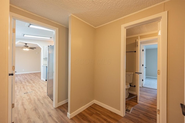 hallway featuring crown molding, a textured ceiling, and light hardwood / wood-style floors