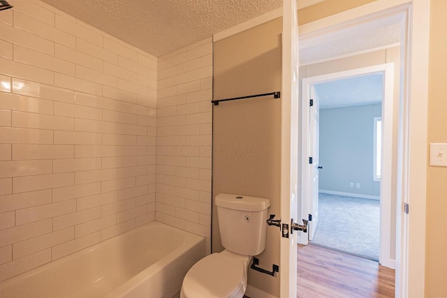 bathroom featuring wood-type flooring, toilet, tiled shower / bath combo, and a textured ceiling