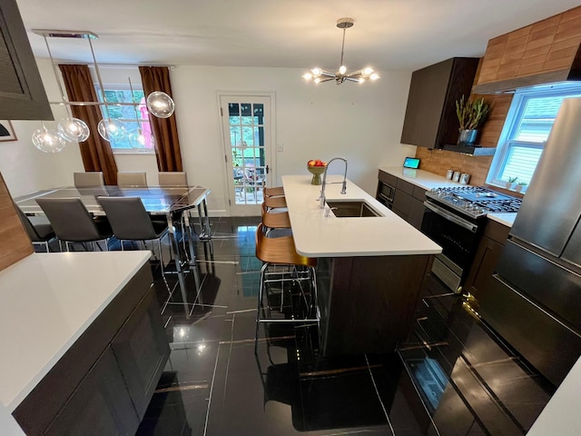 kitchen featuring pendant lighting, sink, a chandelier, a kitchen island with sink, and stainless steel range with gas stovetop