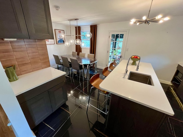 kitchen with pendant lighting, a breakfast bar, an inviting chandelier, an island with sink, and decorative backsplash