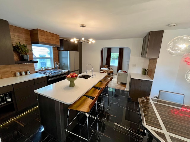 kitchen with sink, a breakfast bar area, refrigerator, an island with sink, and gas range oven